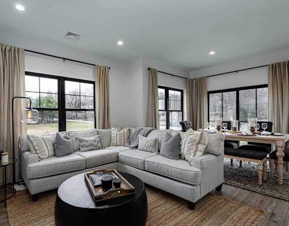 A modern living room with a grey sofa, a coffee table, and a dining table set up.