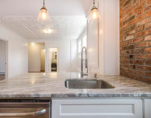 A kitchen with a marble countertop and a brick wall.