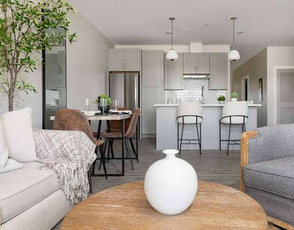 A living room with a grey couch, a wooden table, and a white vase on it.