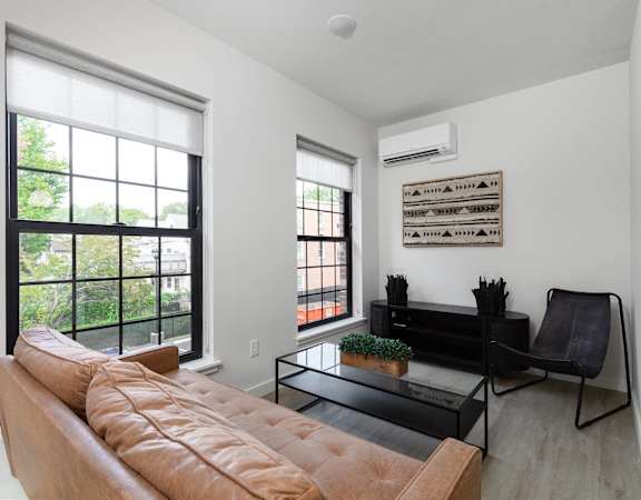 A living room with a brown couch, a black coffee table, and a window with a view of trees.