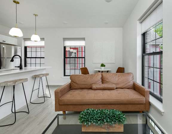 A brown couch is in the middle of a white room with a glass table in front of it.