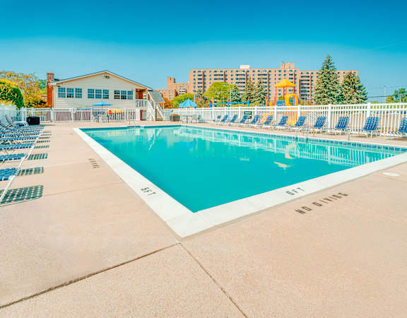 A large outdoor swimming pool surrounded by a white fence and lounge chairs.