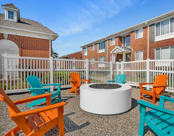 A white fire pit sits in the middle of a patio surrounded by colorful chairs.