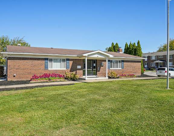A small brick house with a front porch and a green lawn.