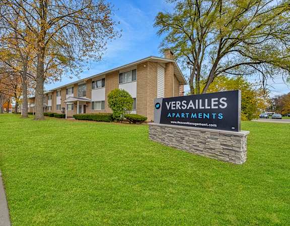 A sign for Versailles Apartments stands in front of a building.