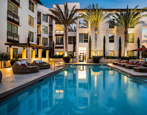 Twilight poolside view with glowing water, lush landscaping, and stylish lounge seating for relaxation
