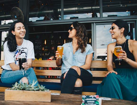 three women sitting on a bench drinking beer at Switchback on Platte Apartments, Littleton, CO