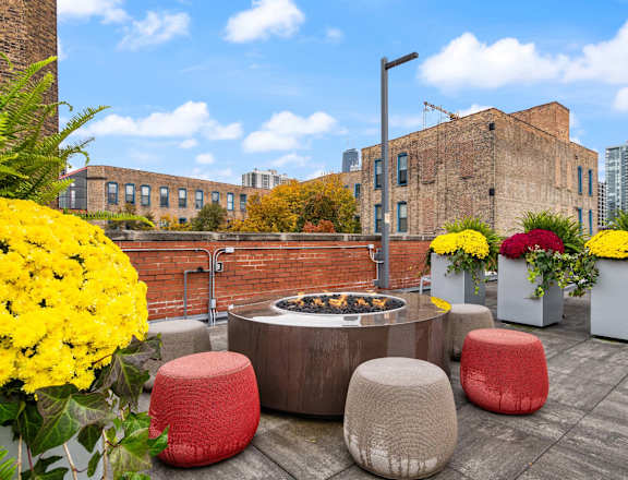 A patio with a fire pit and seating area with flowers.