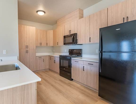 A kitchen with wooden cabinets and a black refrigerator at Woodburn Place Apartment Homes, Woodburn, OR, 97071