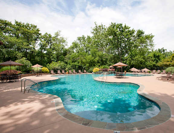 A large outdoor swimming pool surrounded by trees and lounge chairs at Rivercrest Apartments, Piscataway