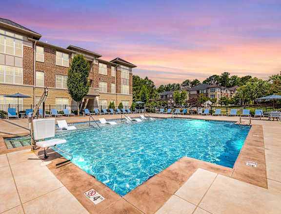 A large swimming pool in front of a building with sun loungers.