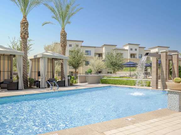 A pool surrounded by palm trees and lounge chairs.