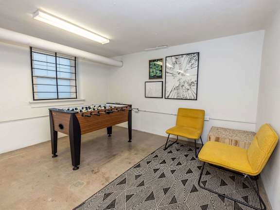 A room with a foosball table, two chairs, and a bench.