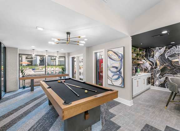 A pool table is in the middle of a room with a ceiling fan and a chair.
