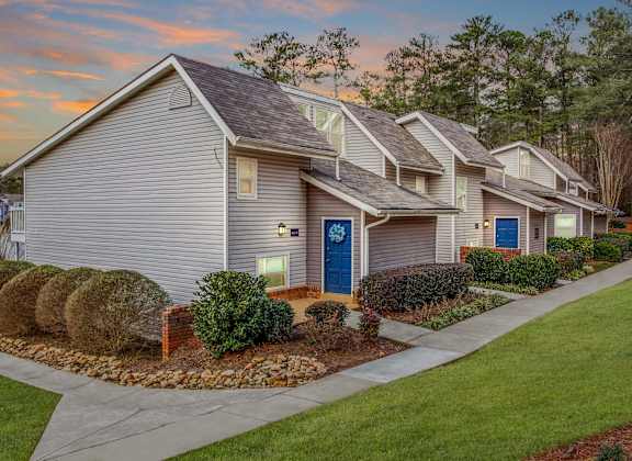 A house with a blue door is surrounded by bushes and a stone pathway.