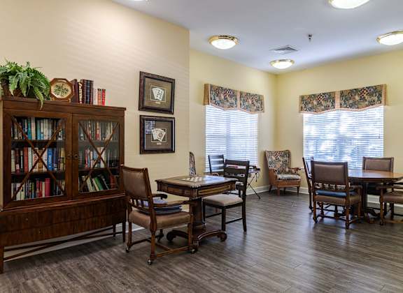 A room with a wooden floor, a bookcase, a table with chairs, and pictures on the wall.at The Gardens of Stafford, Virginia, 22556