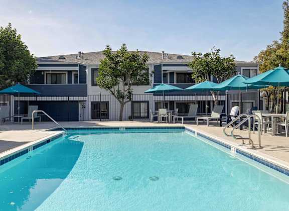 A swimming pool with a blue umbrella and a building in the background.