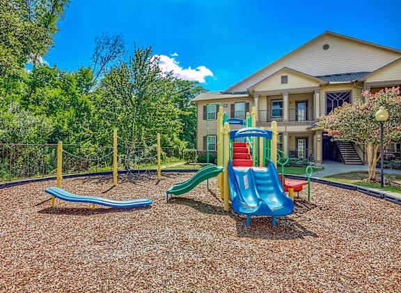 A playground with a slide, swings, and a seesaw in front of a house.