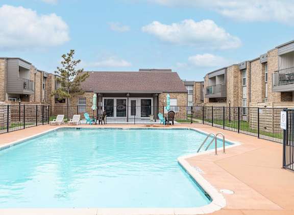 A swimming pool surrounded by a black fence and chairs.