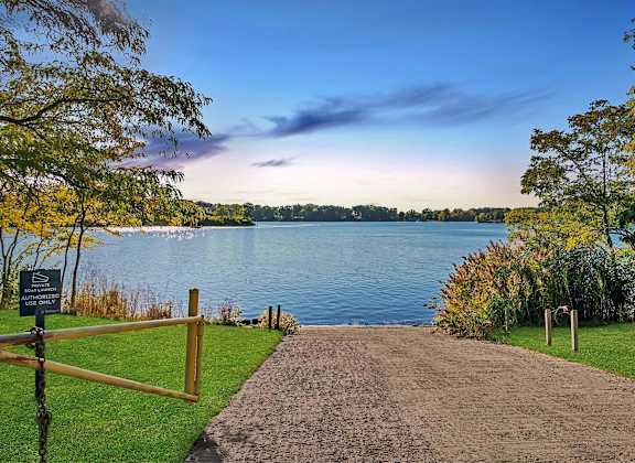A pathway leads to a body of water with a sign on the left.