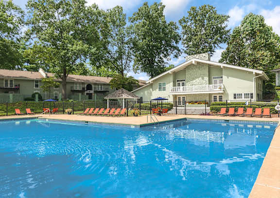 A swimming pool in front of a house with trees in the background.