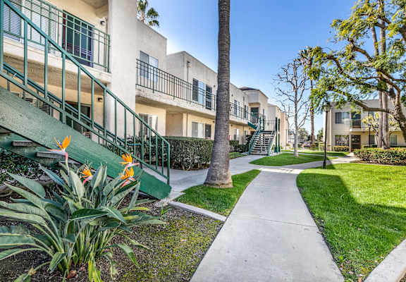 A pathway leads through a grassy area between two rows of apartment buildings. at Whispering Fountains Lakewood, California, 90805