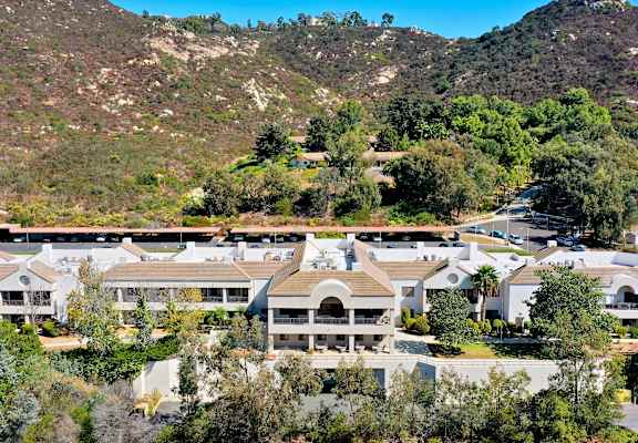 A large white building with a balcony is surrounded by trees and hills.