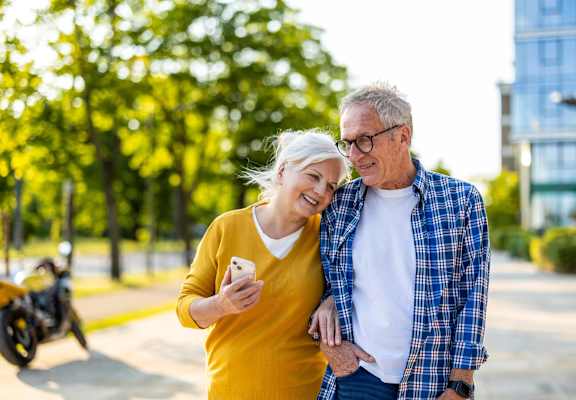 An older couple is standing outside, with the woman holding a phone.