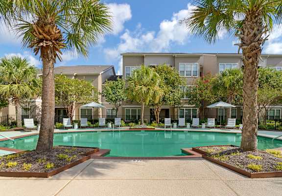 a swimming pool with palm trees and a building in the background at Summerwind in TX 77584
