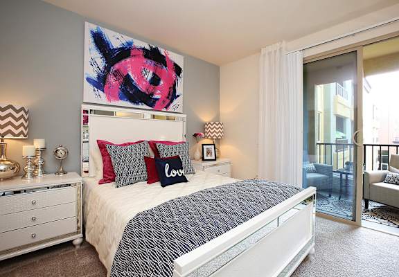 A bedroom with a large bed, a painting above it, and a chair in the doorway at The Kitt at Warner Center in Woodland Hills, 91303
