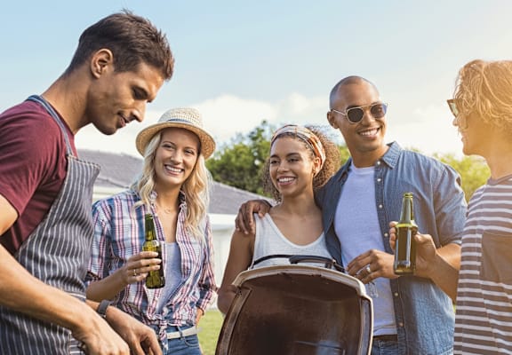 A group of friends are gathered around a barbecue grill, enjoying a sunny day outdoors. at Spring Meadow Apartments, Glendale, AZ, 85302