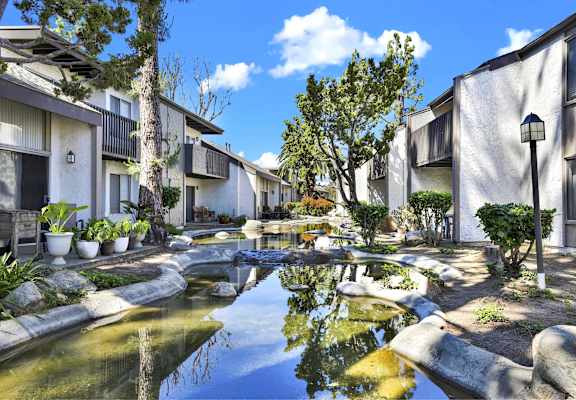 A serene courtyard with a pond and apartment buildings at THE STREAMS Apartments, California