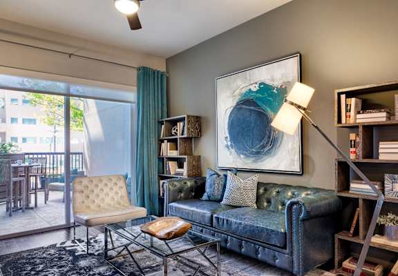 A living room with a blue couch, a chair, a table, and a painting on the wall.