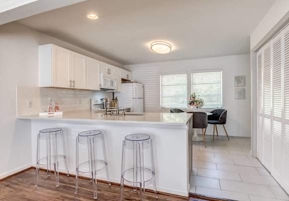 a kitchen with white cabinets and a bar with three stools