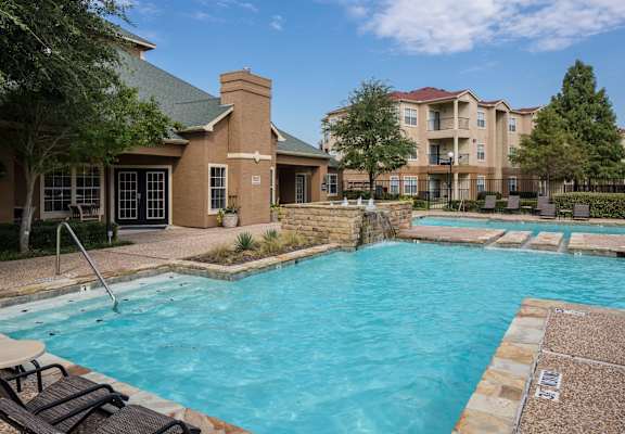 A large outdoor swimming pool with a stone border and a small patio area with chairs and a table. at Infinity on Sunnyvale Apartments , Mesquite, 75150