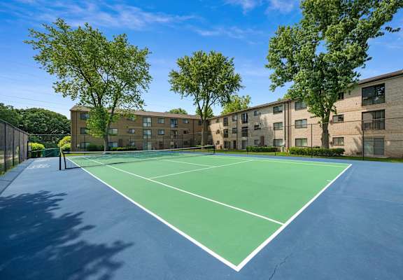 a tennis court with trees and apartments in the background