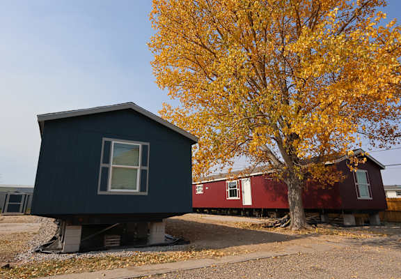 a black house with a red house behind it next to a tree at Country Lane, Cheyenne, Wyoming