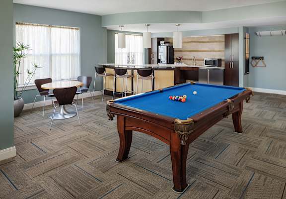 A pool table in a room with a bar and kitchen in the background.