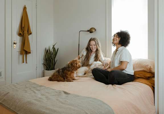 Two women sitting on a bed with a dog.