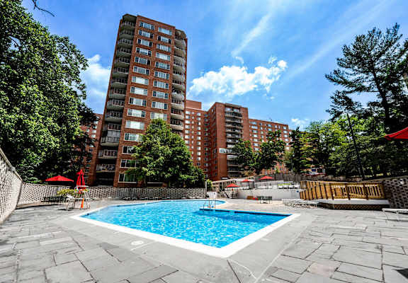 A swimming pool surrounded by a stone patio and trees with a red umbrella and chairs.