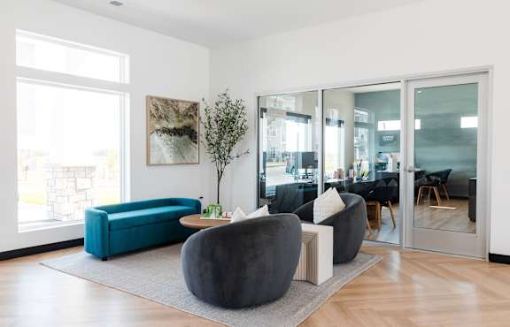 A living room with a blue couch and a grey ottoman.at Converge NW, Waukee, IA 50263