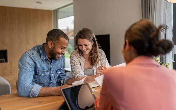 Three people are sitting at a table with papers and a laptop.