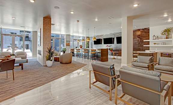 The amazing resident lounge with gray and white couches, plants, decorations, large windows, unique overhead lighting, plush chairs, three flatscreen TVs, a bar counter with barstools and coffee tables at the Ritz Classic Apartment Homes. 