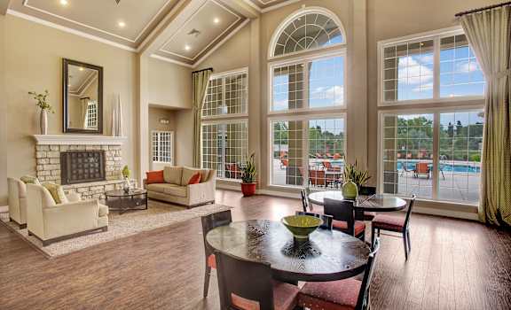The resident lounge with a fireplace, couches, decorations, plush chairs, coffee tables, and windows that overlook the pool at Legends at River Oaks Apartments. 