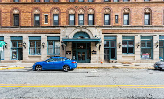 A blue car is parked in front of a building with a green awning.