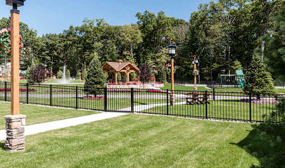 A black fence surrounds a grassy area with a lamp post and a gazebo in the background.