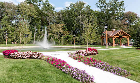 A garden with a fountain and a house in the background.