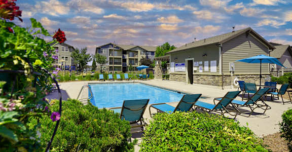 A pool surrounded by lawn chairs and flowers with a building in the background.at Florentine Villas, Midvale Utah