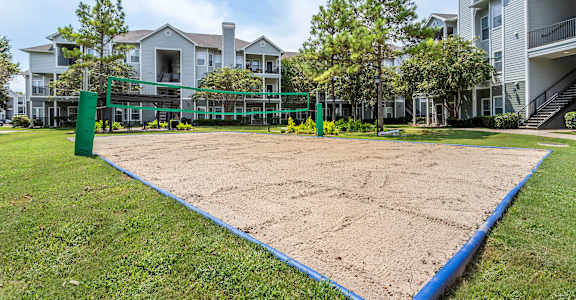 A sand volleyball court is surrounded by a green fence and blue border  at Reserve by the Lake, TX, 77084