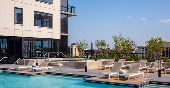 A swimming pool with sun loungers and a building in the background.